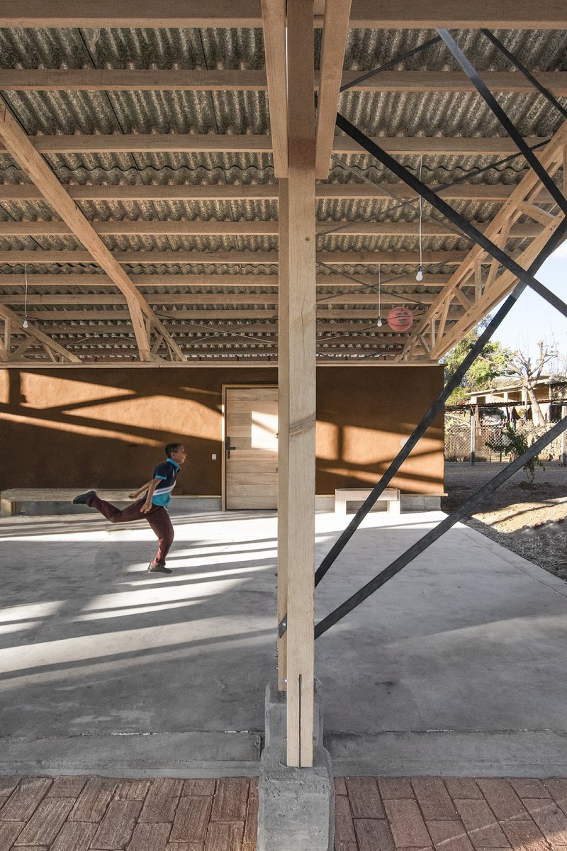 View through timber columns and diagonal steel bracing with child playing on concrete floor below