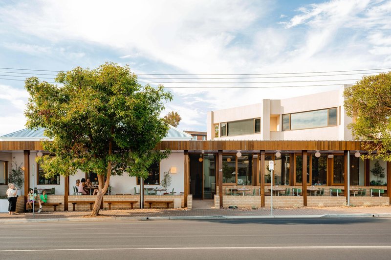 Street facade with timber-clad ground floor and white upper volume framed by established trees