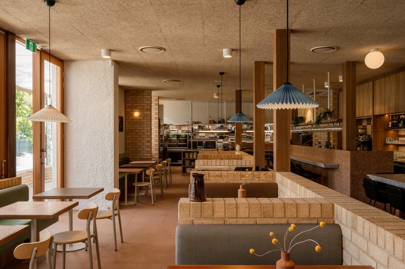 Dining interior showing pale brick service counter and timber columns beneath cork acoustic ceiling panels