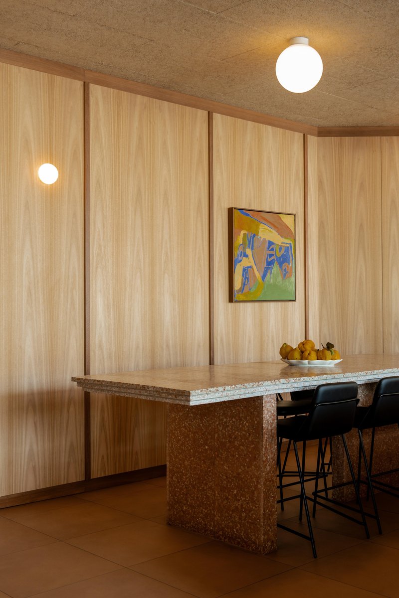 Terrazzo island counter with timber edge against vertical wood paneling and globe ceiling fixture