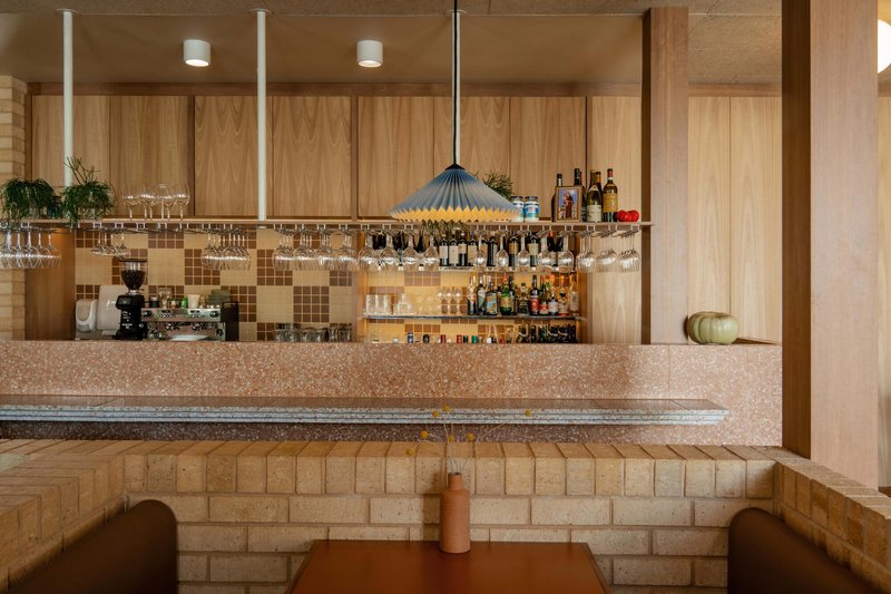 Bar counter with suspended glass rack and mosaic tile backsplash beneath recessed ceiling lights