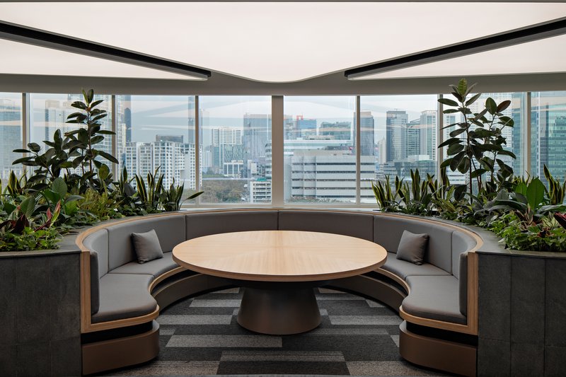 Circular banquette seating around a timber table with integrated planter beds along the curved perimeter