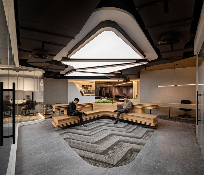 Reception area with tiered timber seating, triangular ceiling light fixtures, and patterned chevron carpet inlay