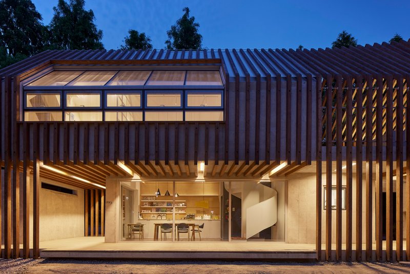 Glass-walled dining area framed by vertical timber louvers and clerestory windows at blue hour