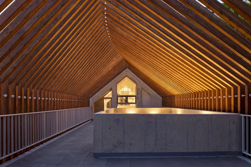 Covered walkway with rhythmic timber slat ceiling and concrete reception desk at twilight