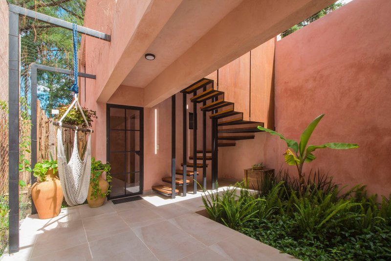 Covered terrace with open-tread steel staircase, potted plants and dappled midday sunlight
