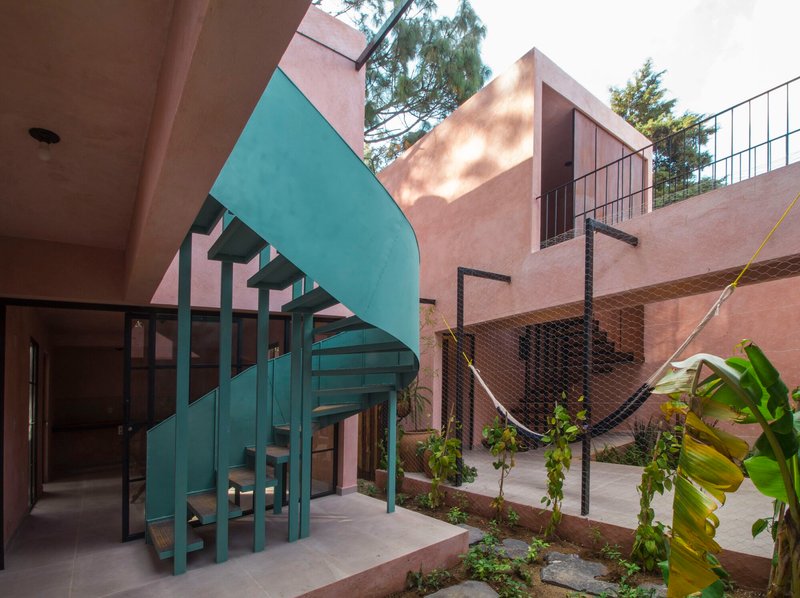 Courtyard view showing the teal spiral stair, hammock netting, and pink stucco volumes in dappled sunlight