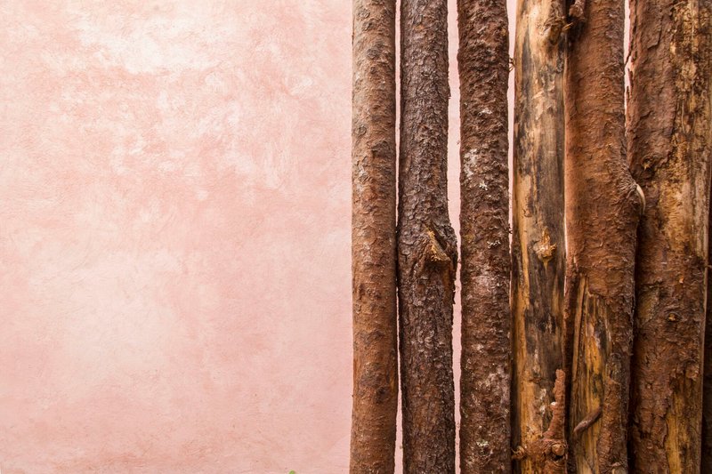 Detail of vertical bamboo poles meeting pink stucco wall at weathered junction