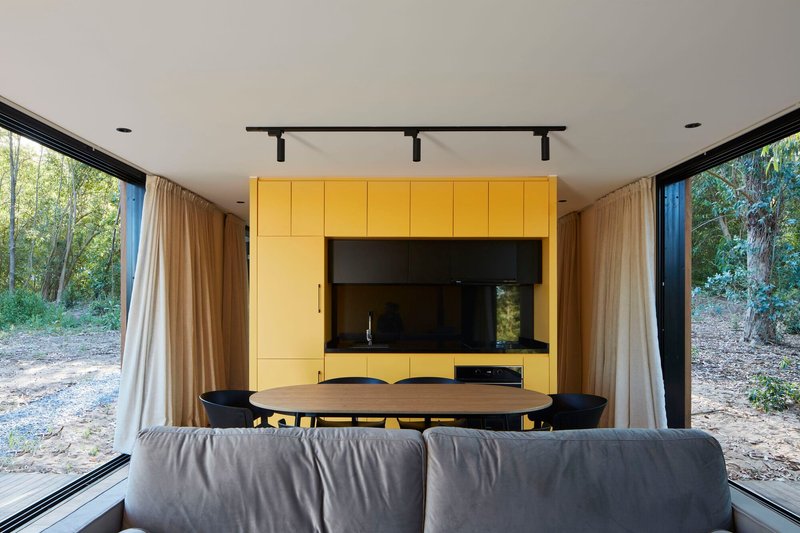 Interior view of the dining area with yellow cabinetry and full-height glazing opening to the forest