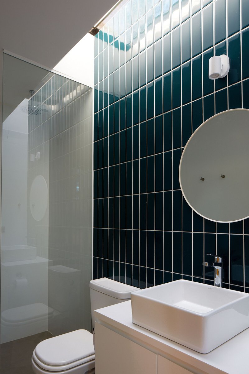 Bathroom with vertical dark green tile wall, skylight above, and wall-mounted circular mirror beside sink