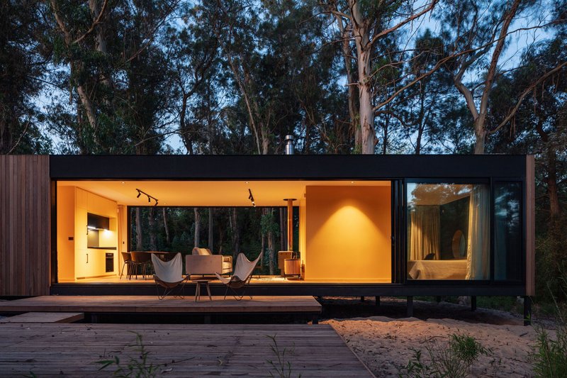 Timber deck extending from the fully glazed living volume with warm interior lighting at twilight