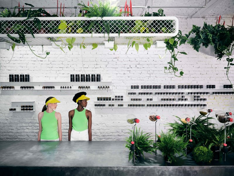 Wall-mounted mesh planter with trailing vines above white brick and product display shelves with two visitors below