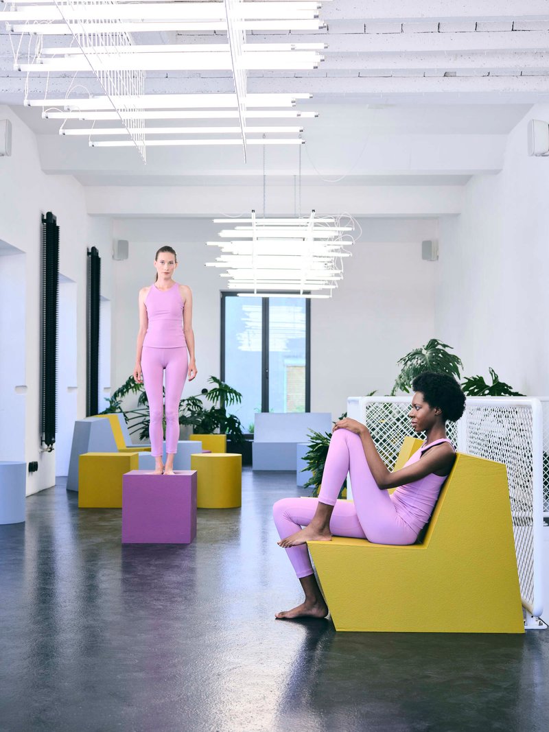 Interior room with suspended white tube lighting fixture, colored geometric seating blocks, and two occupants