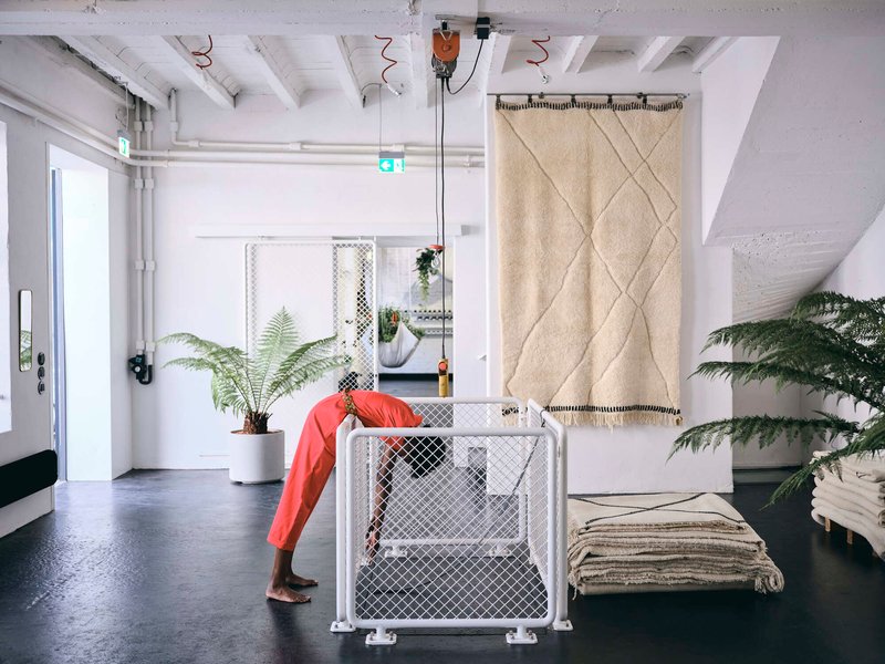 Interior view of white space with exposed ceiling beams, wire mesh partitions, potted ferns and a person in red