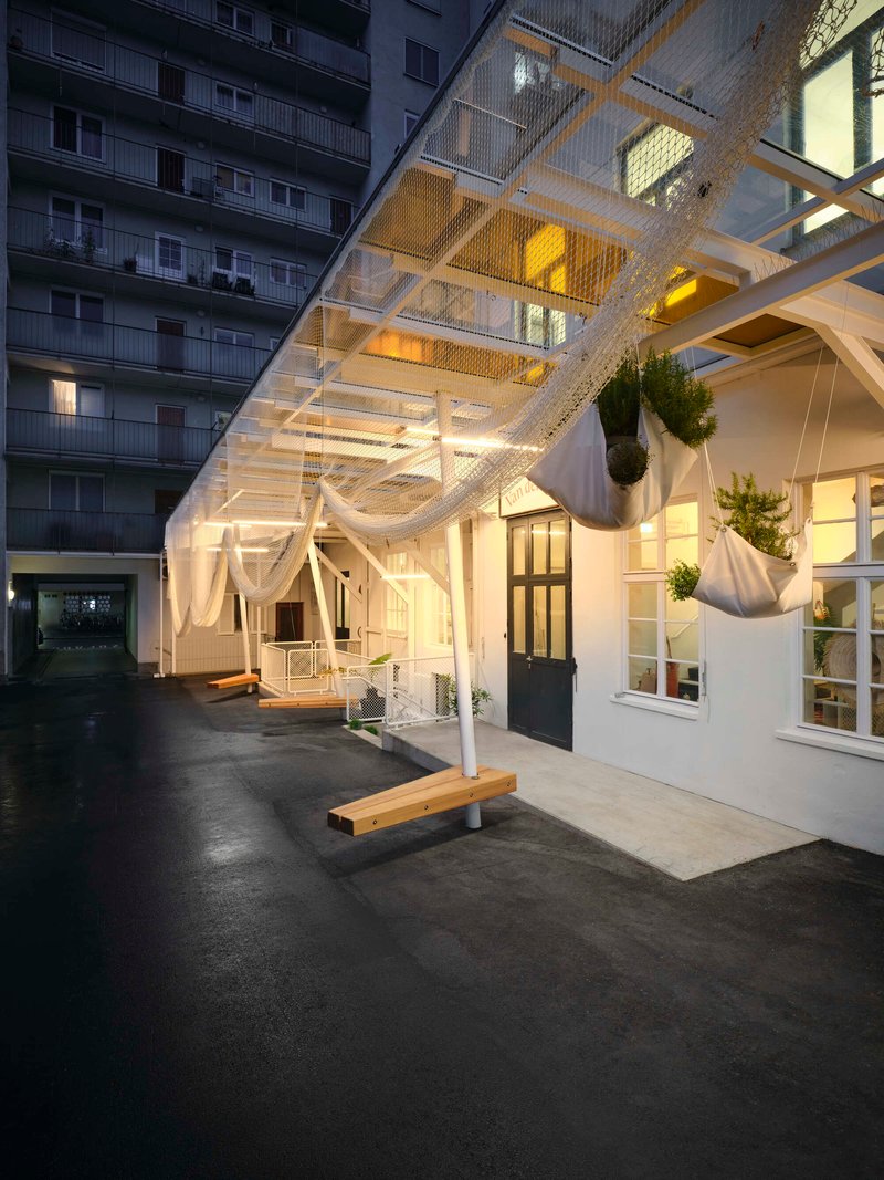 Courtyard at dusk showing illuminated white metal canopy structure with hanging planters and adjacent apartment tower