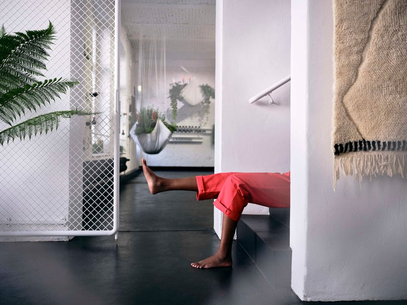Person's legs resting against white column with suspended planters and wire mesh partition in background