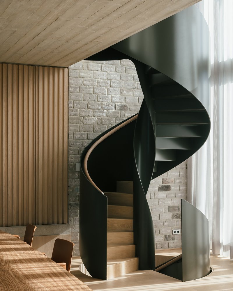 Black metal spiral staircase with timber treads against a white brick wall with vertical timber panels