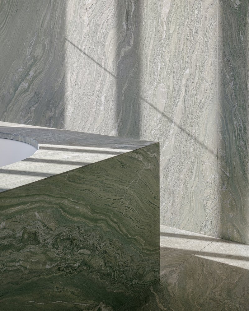 Green veined marble block meeting pale stone wall with angular shadows cast across the surfaces