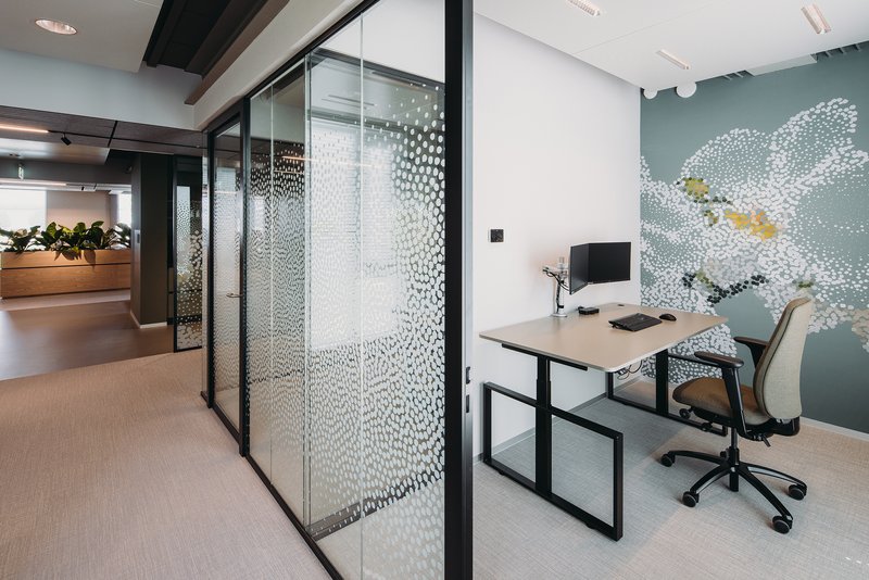 Office workstation beside black-framed glass partitions with dotted film pattern and wall mural beyond
