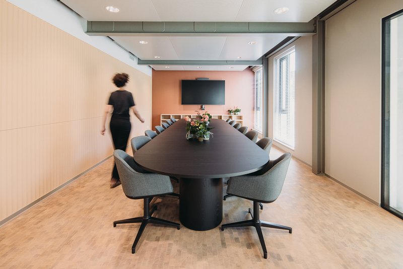 Conference room with oval dark table and person walking past warm terracotta accent wall