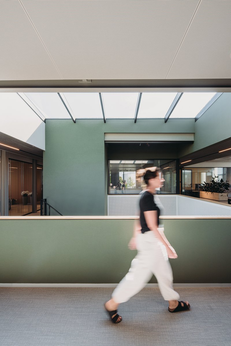 Mezzanine walkway with mint green guardrail and a person in motion beneath perforated ceiling panels