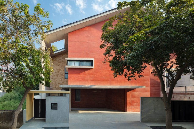 Street view of the red sandstone facade with narrow windows framed by mature trees on both sides