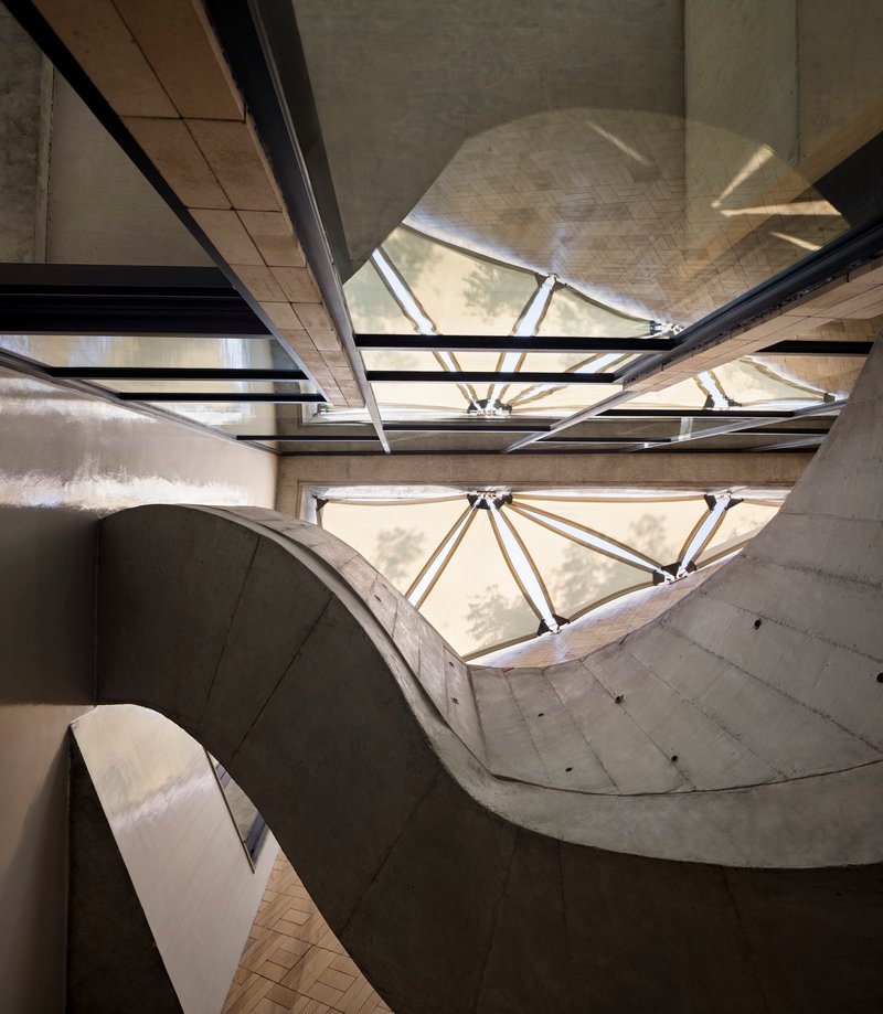 View looking up at the concrete stairwell with triangular skylights and steel bracing overhead