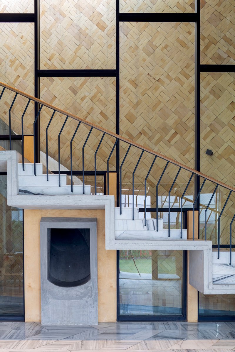 Black metal staircase with curved railing rising past herringbone bamboo wall panels and fireplace surround