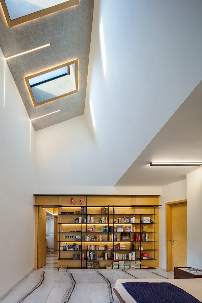 Double-height library space with skylights, timber bookshelves, and recessed cove lighting along white walls
