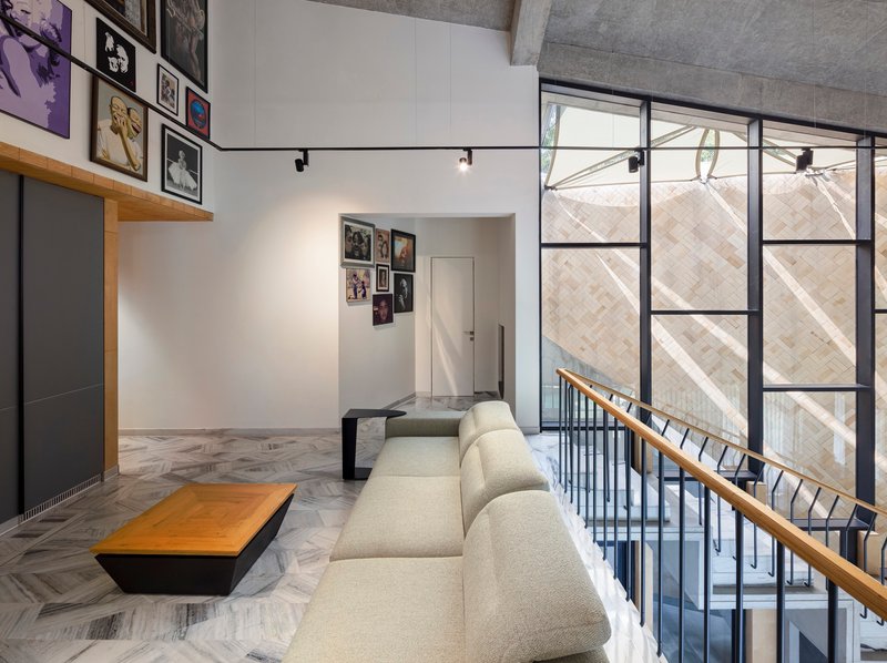 Double-height living space with steel-framed glazing overlooking a diagonal brick facade and exposed concrete ceiling