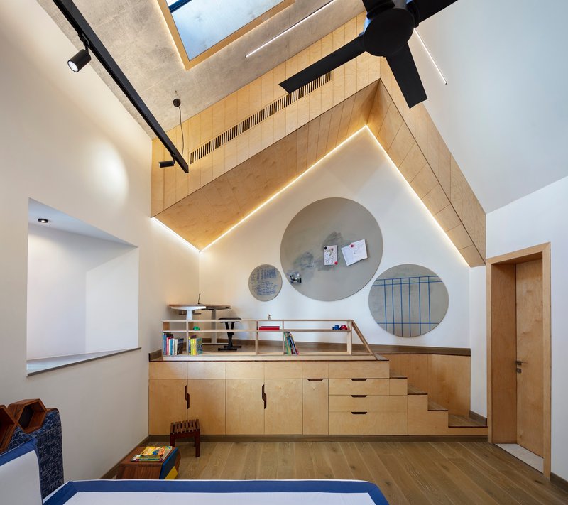 Plywood loft platform with circular wall niches and built-in storage cabinets under a vaulted ceiling