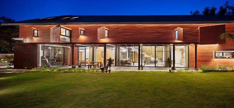 Rear elevation with horizontal timber cladding and continuous glazed openings illuminated at twilight above a lawn