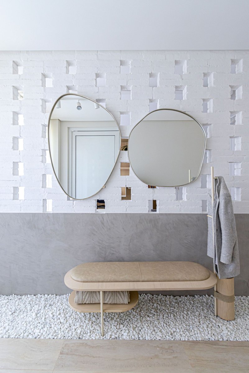 Bathroom vanity with two oval mirrors on white geometric tile above a timber bench
