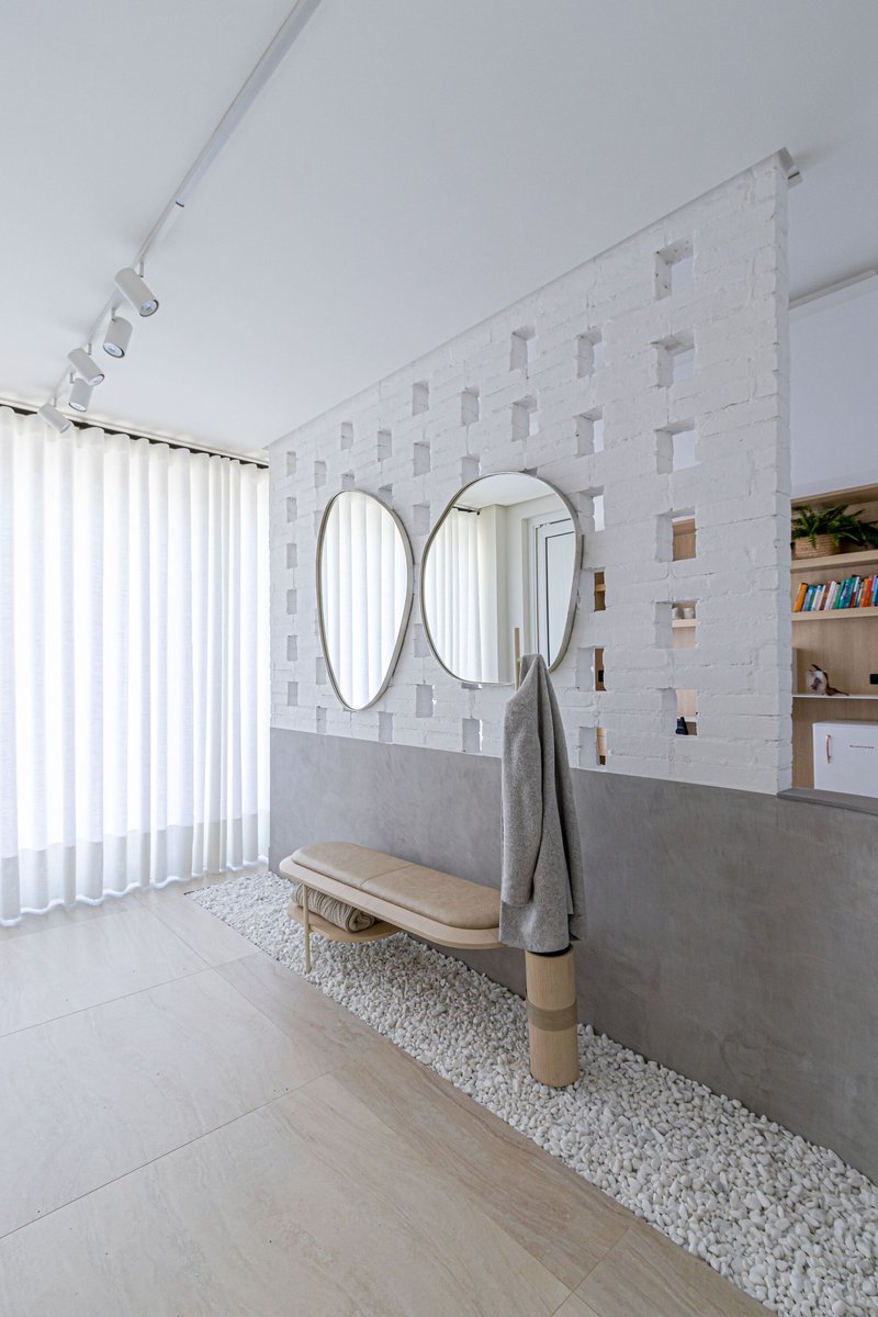 Interior wall with textured white tile and three oval mirrors above a concrete ledge with white pebbles