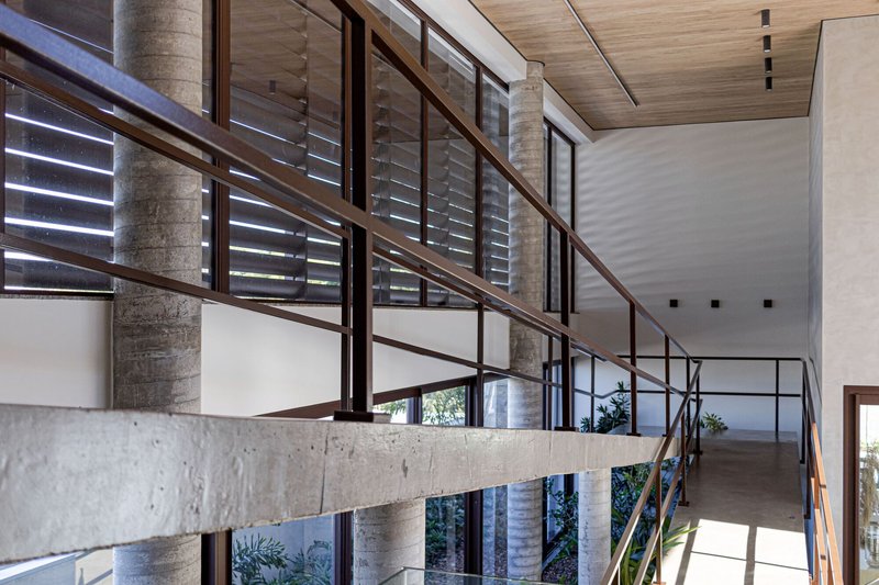 Exposed concrete beam supporting a walkway with louvered windows and metal railings above planted beds