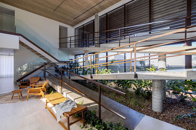 Double-height interior with sunken planted bed, metal railings and timber ceiling under afternoon light