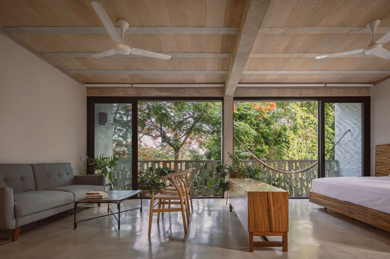 Living space with exposed concrete beams opening onto lattice-screened terrace with lush vegetation