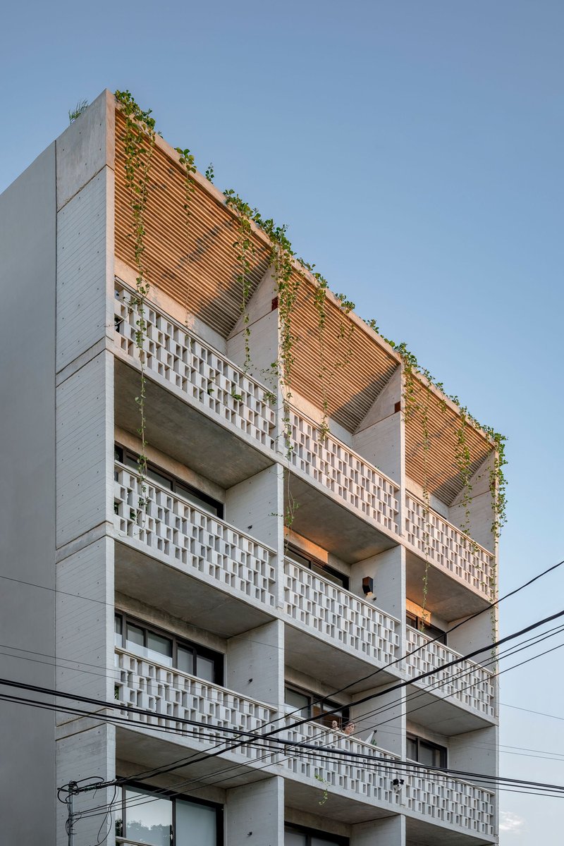 Upper levels showing timber louver screens and perforated concrete balcony railings under clear sky