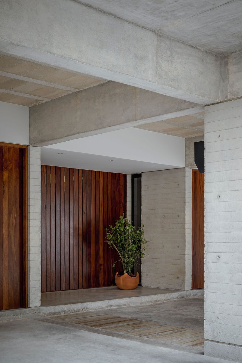 Entry threshold with vertical timber door panels and potted plant against board-formed concrete walls