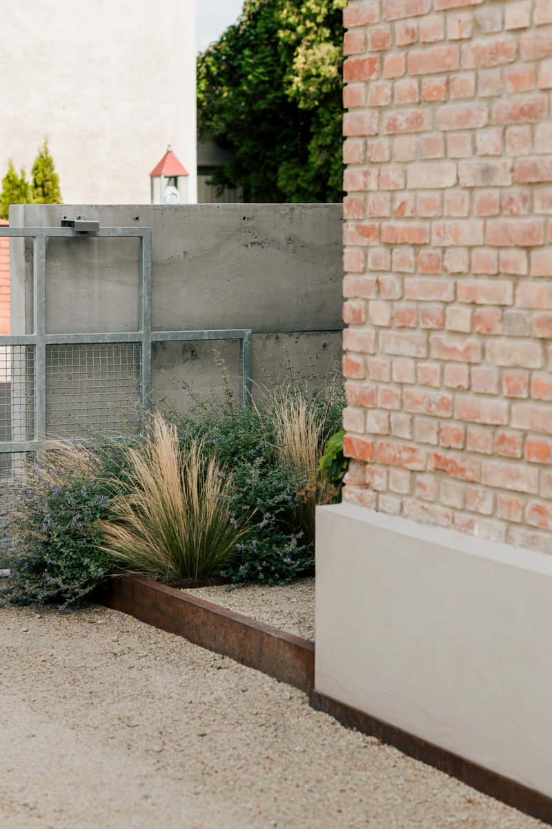 Garden view showing concrete wall and brick facade with planted grasses in corten-edged bed