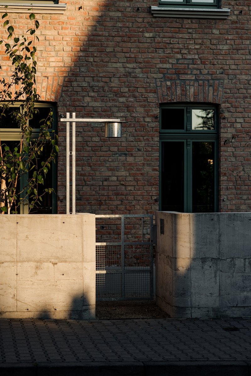 Red brick facade with concrete base wall and metal mesh gate in low afternoon sunlight