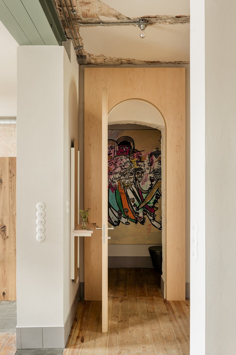 Arched plywood doorway revealing a bathroom alcove with exposed ceiling beams and colorful mural