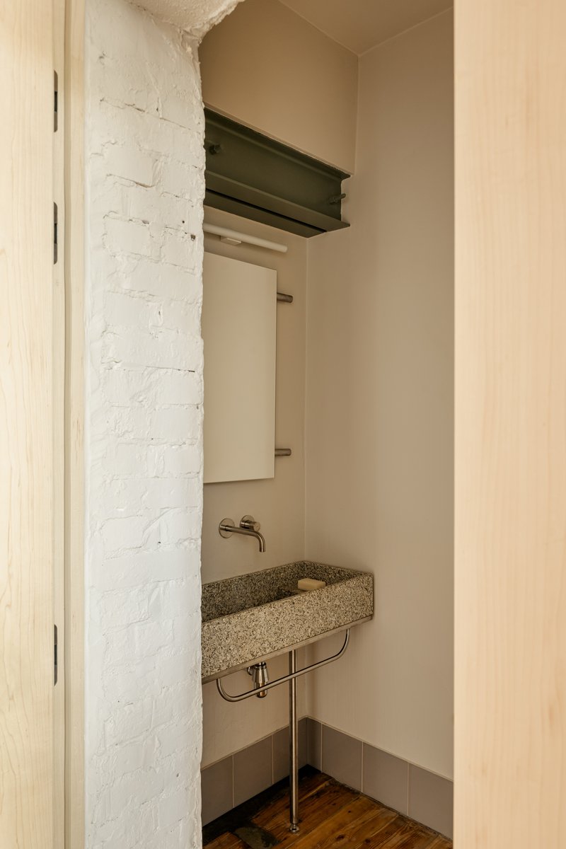 Compact powder room with terrazzo basin on metal stand beside painted brick wall