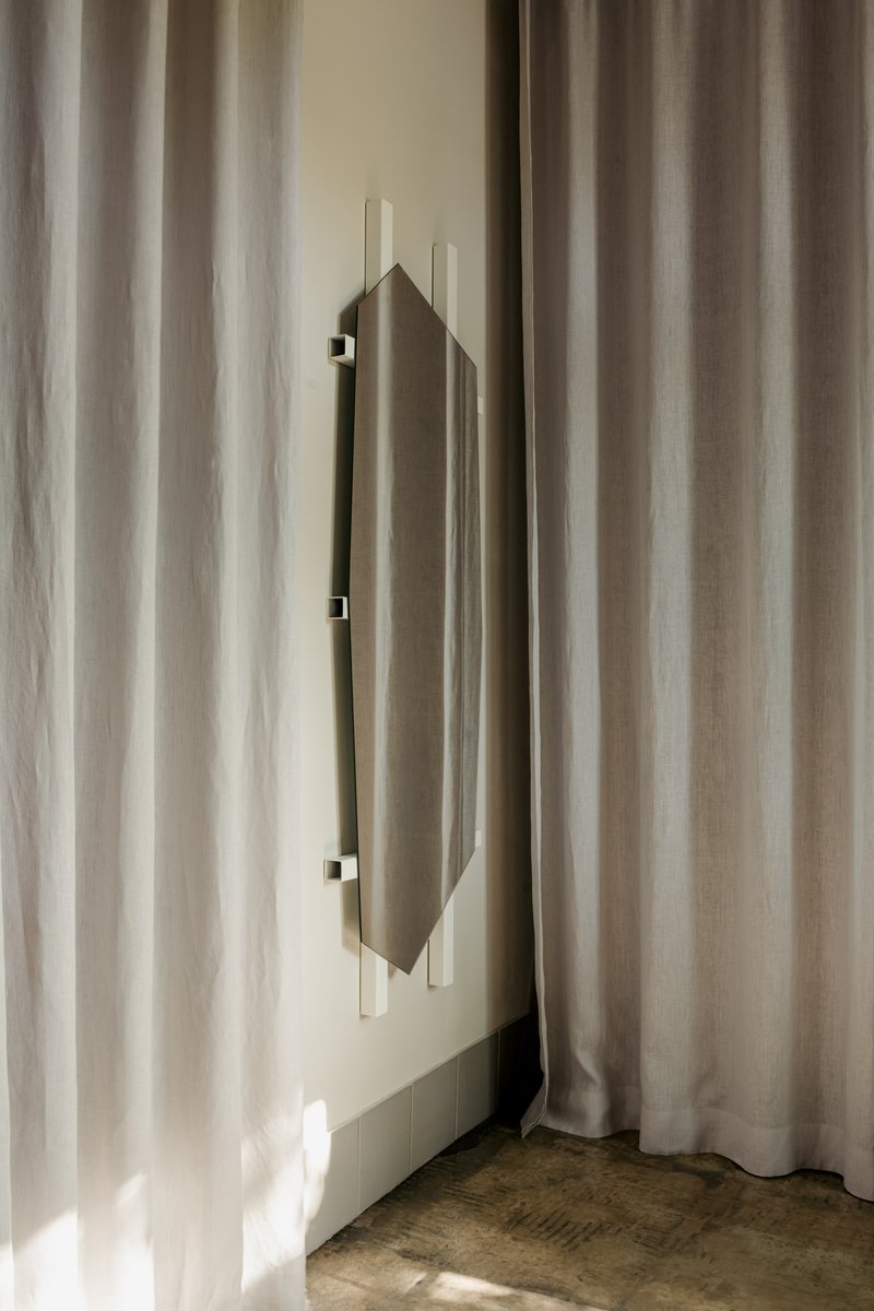 Vertical door pull on pale wall framed by sheer curtains in soft daylight