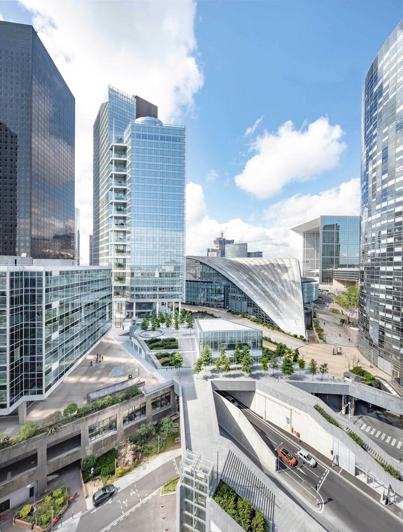 Plaza level with planted terraces and curved shell roof between glass towers on a sunny day