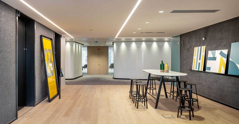 Open lobby with high-top tables and black stools beneath linear ceiling lighting