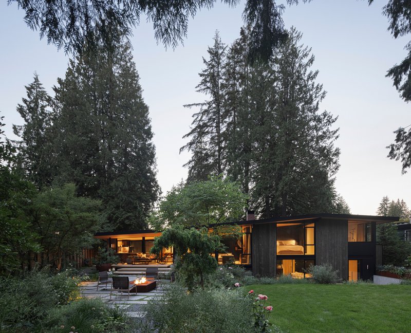 Garden view showing pavilions connected by low roof planes among mature conifers at twilight