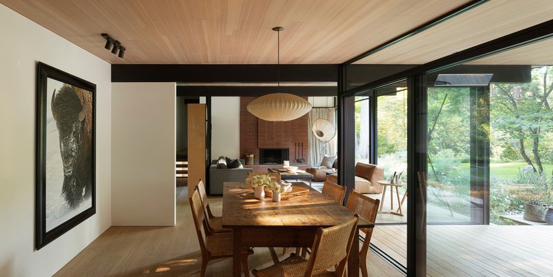 Dining area with floor-to-ceiling glazing overlooking a garden and brick fireplace beyond