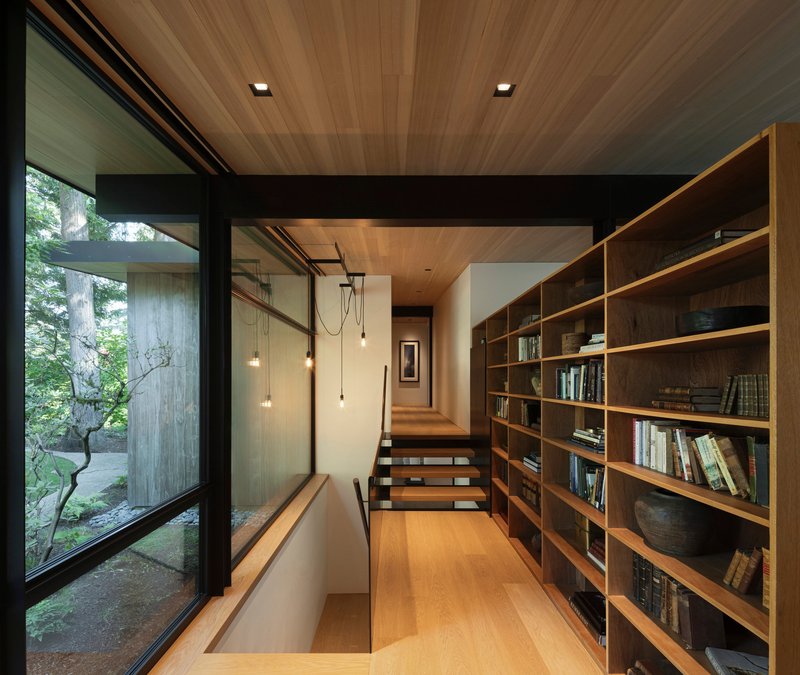 Timber-lined hallway with built-in bookshelf and pendant lights ascending to upper level