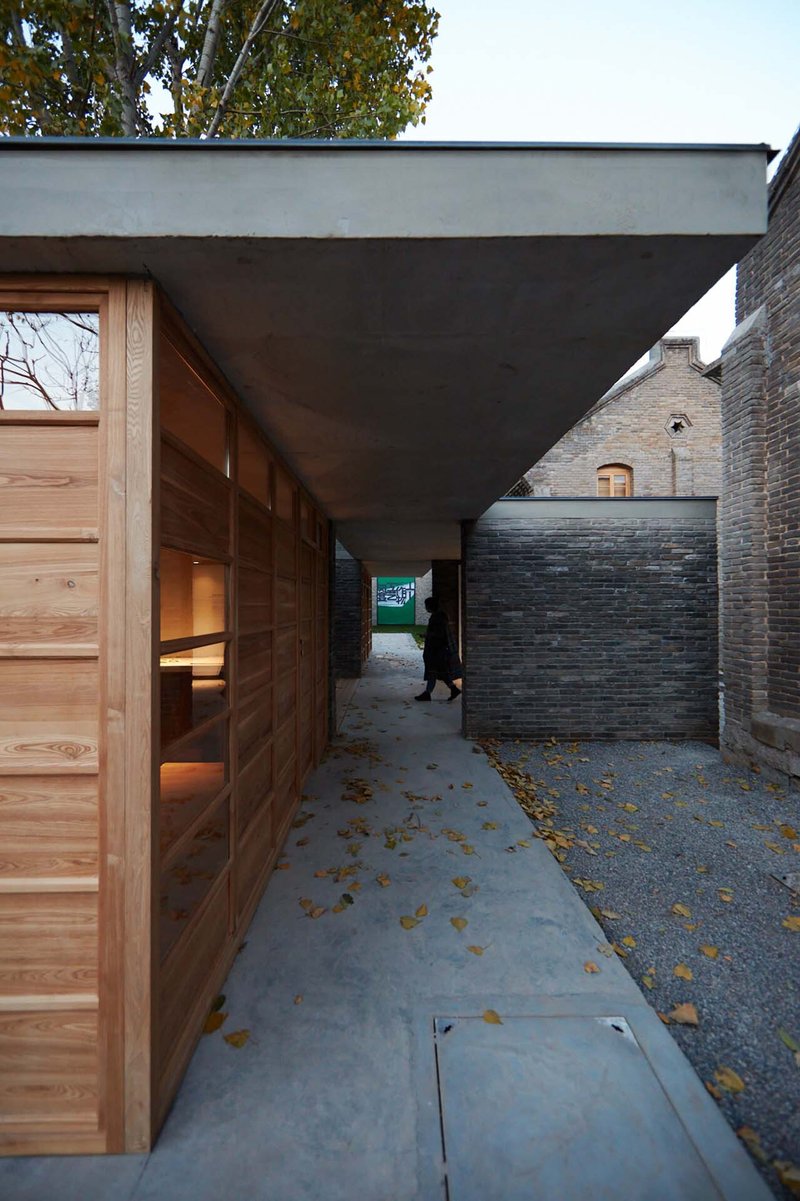 Covered entry passage with timber sliding doors and concrete soffit between brick walls scattered with autumn leaves